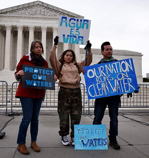 Three people holding signs advocating for clean water and protecting waters