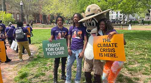 People holding signs and posing for a photo with Ranger Rick in a park