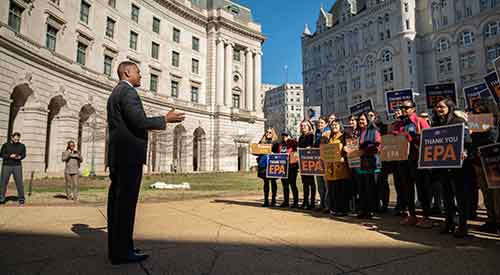 Person speaking in front of crowd holding signs reading Thank You EPA