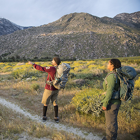 Two hikers on a trail wearing backpacks