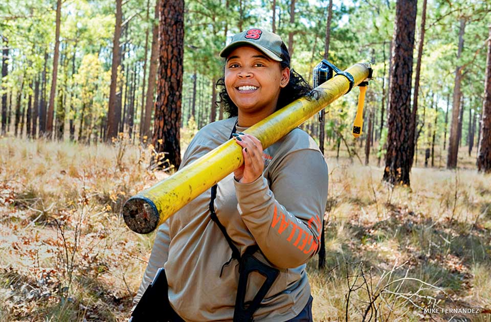 An image of Lauren Pharr posing while holding an extendable pole used to check cavities in trees.