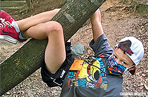 A kid in a mask dangles from a tree 