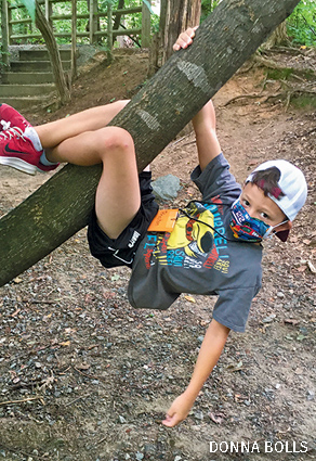 A kid in a mask dangles from a tree